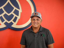 Image of Kevin Riel wearing YCH hat and standing in front of YCH wall with logo etched